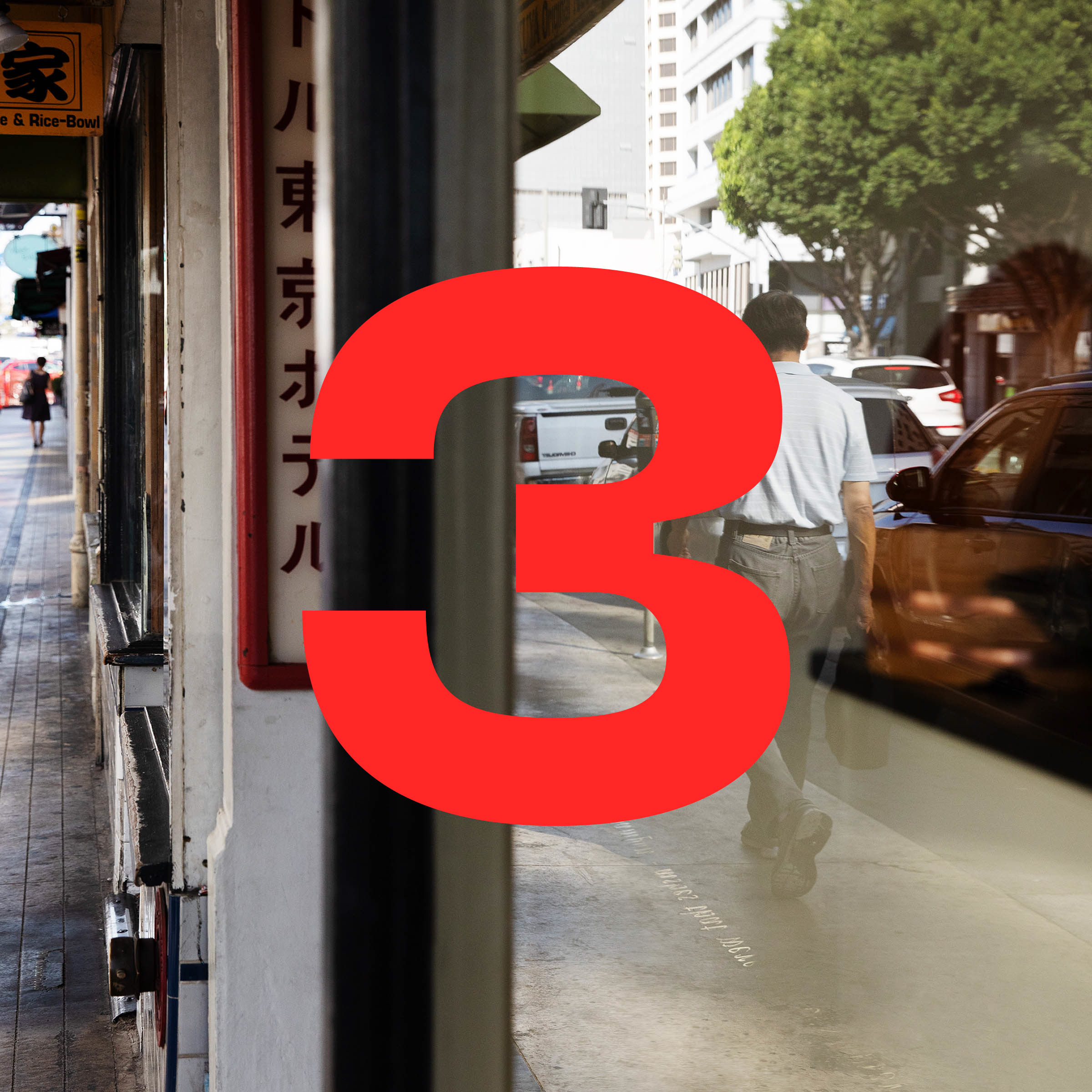 The red numeral 3 is superimposed over a photograph of a city sidewalk. Japanese writing appears on a sign. A shop window reflects traffic, a line of parked cars, and a man walking away from the camera.
