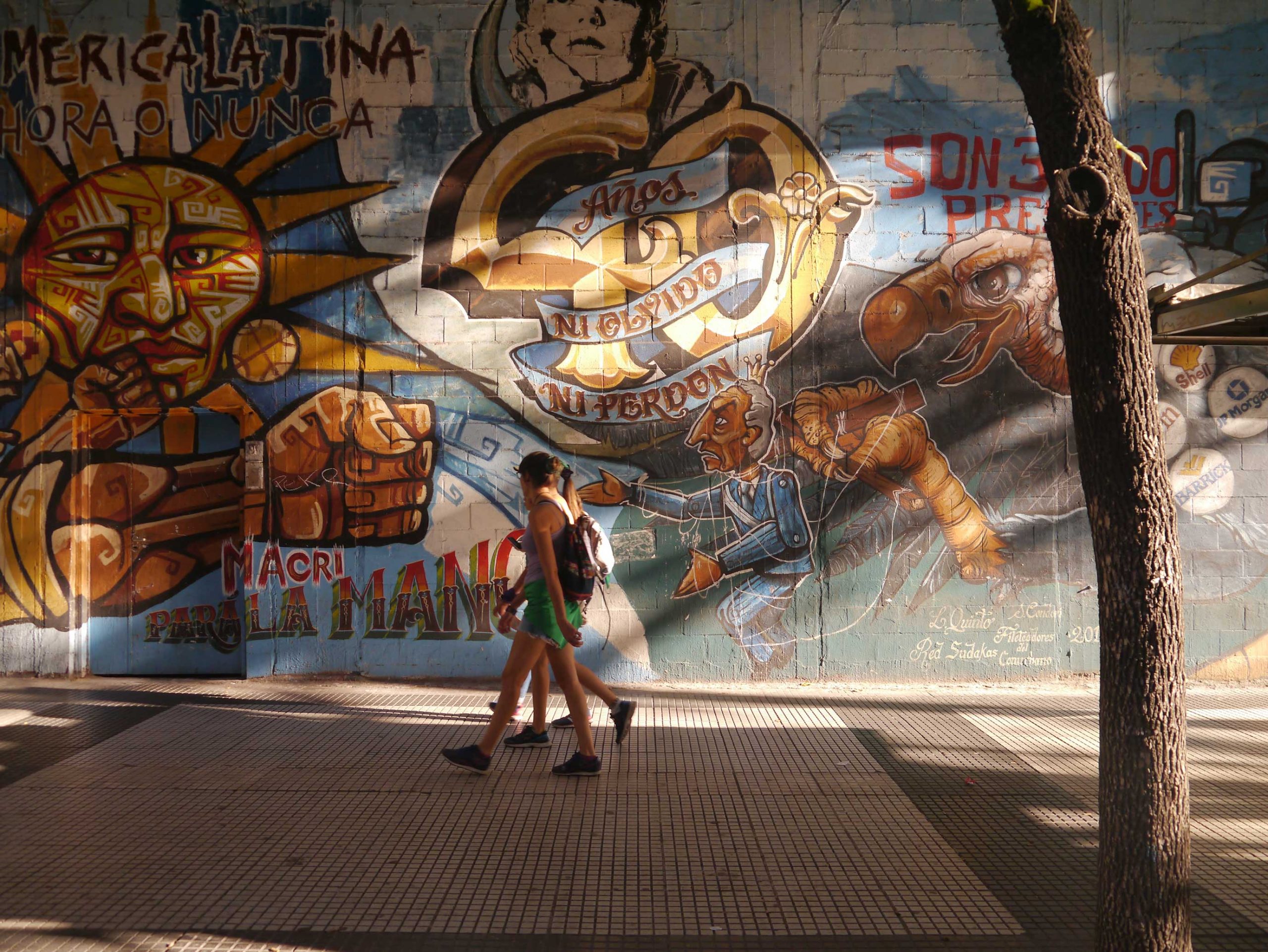 Two young people walking past a wall mural.